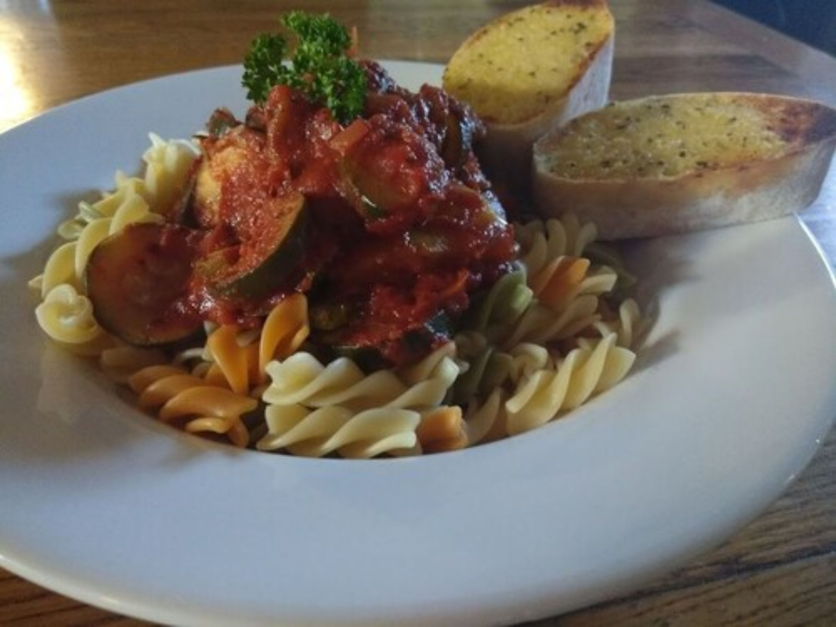 Een bord pasta met tomatensaus, groene bonen en een garnering van peterselie.