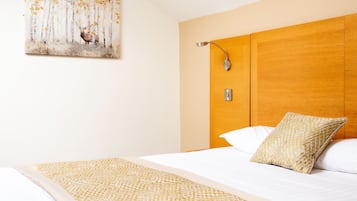 Habitación de hotel con una cama grande, cabecera de madera, luz de pared y un cuadro de un paisaje forestal.