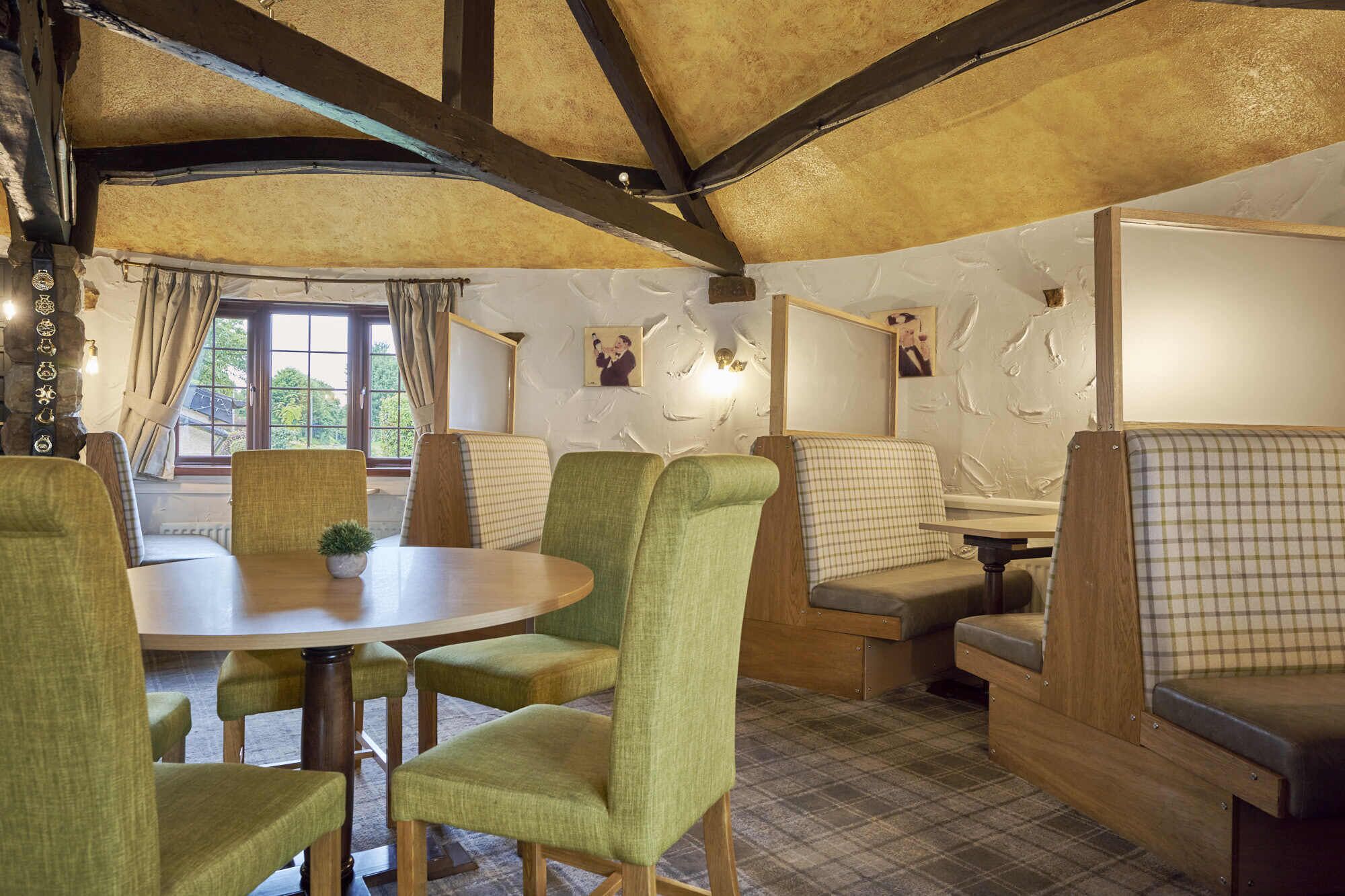 A cozy room with a round table, green upholstered chairs, and a checkered sofa.