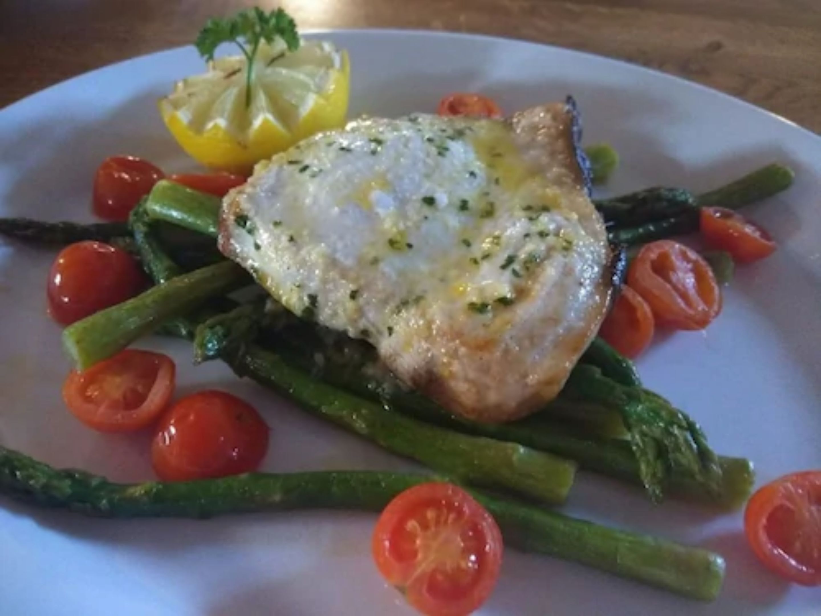 A plate with a piece of fish, asparagus, cherry tomatoes, and a lemon wedge.