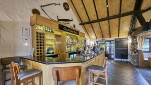 Un rústico espacio de bar con taburetes de madera, una estantería para vinos y un letrero que dice 