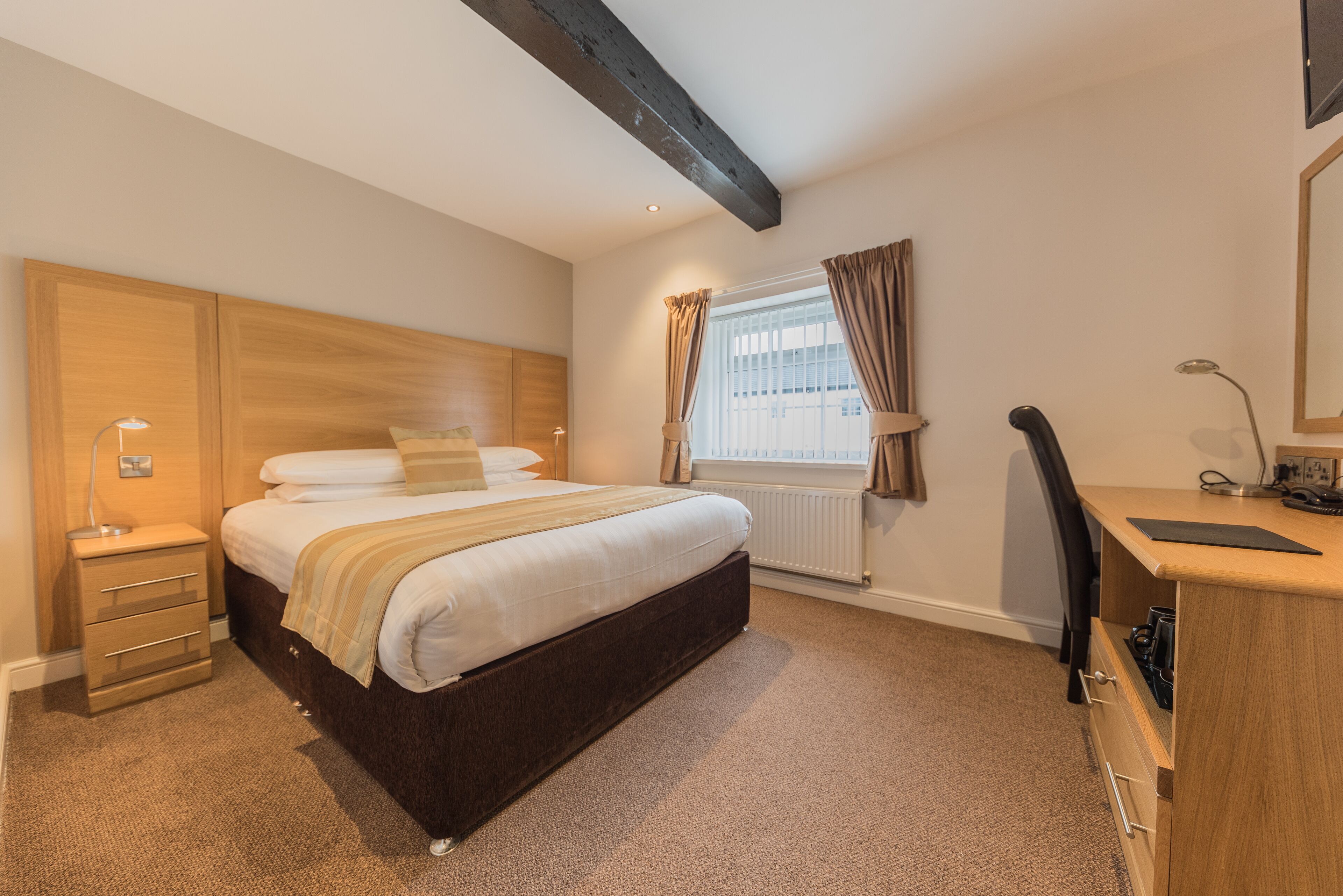 A bedroom with a bed, bedside table, lamp, and a desk with a chair.