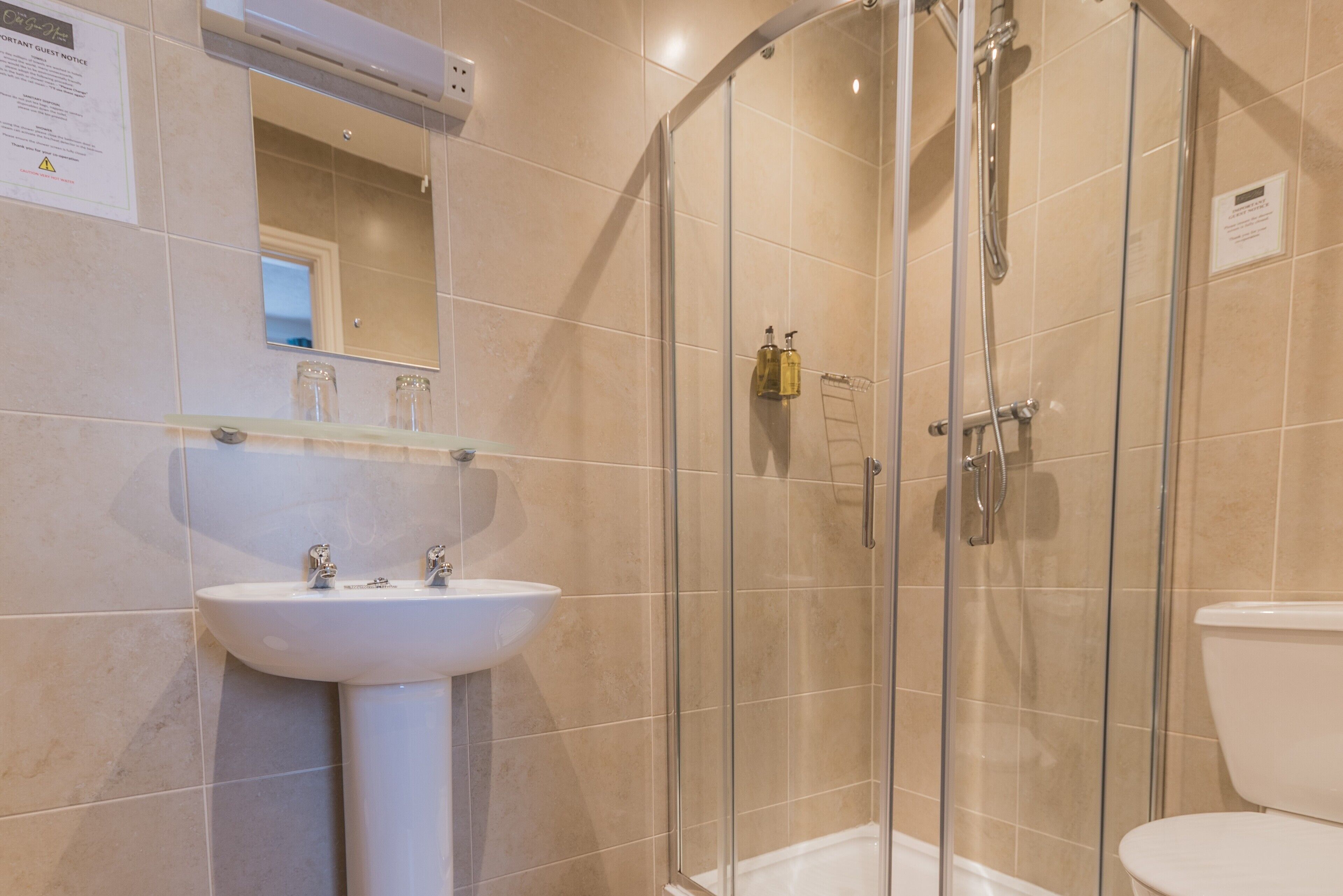 Une salle de bain avec une douche à parois de verre, un lavabo sur colonne et des toilettes.