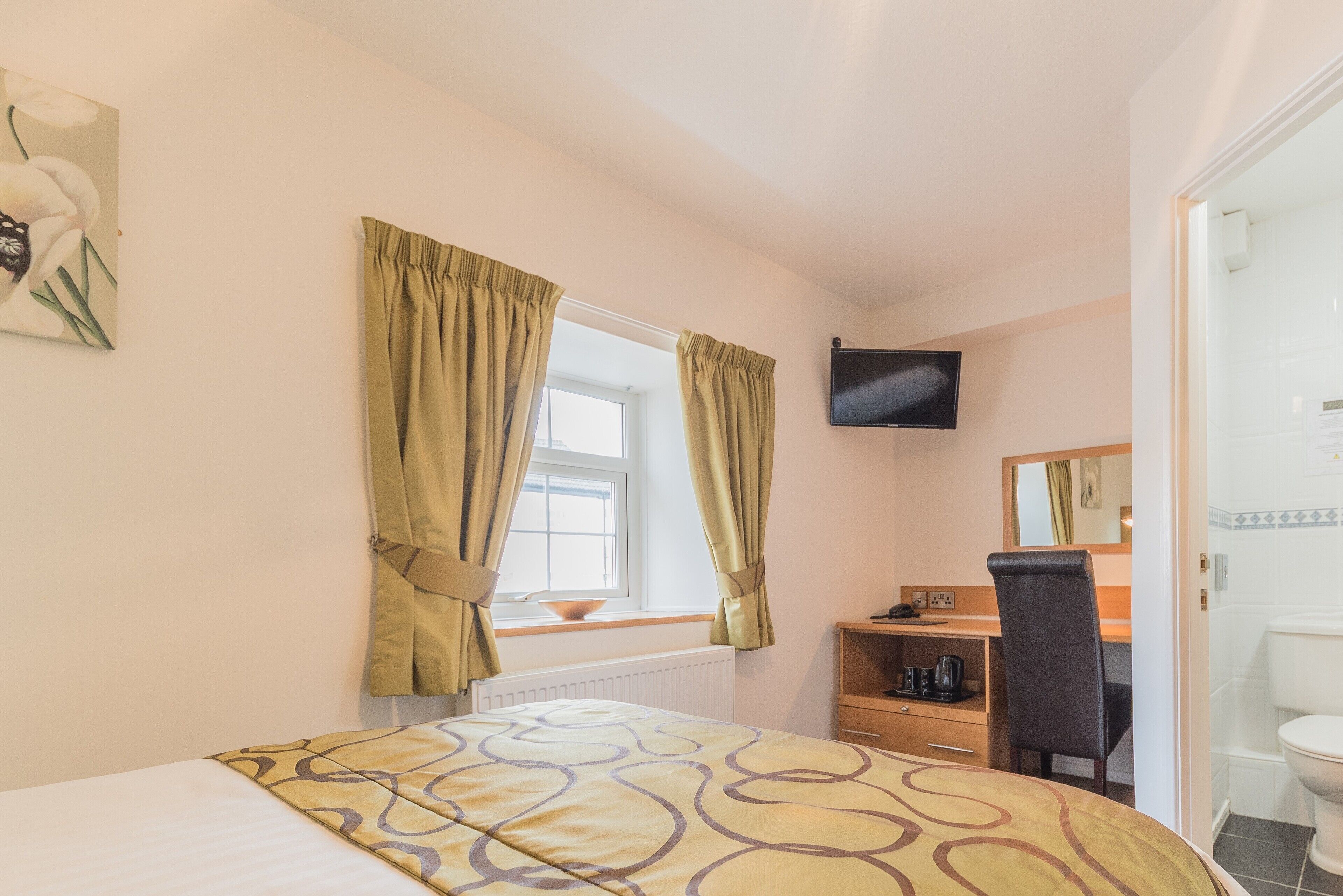 A bedroom with a bed, a desk, a chair, a television, and a window with curtains.