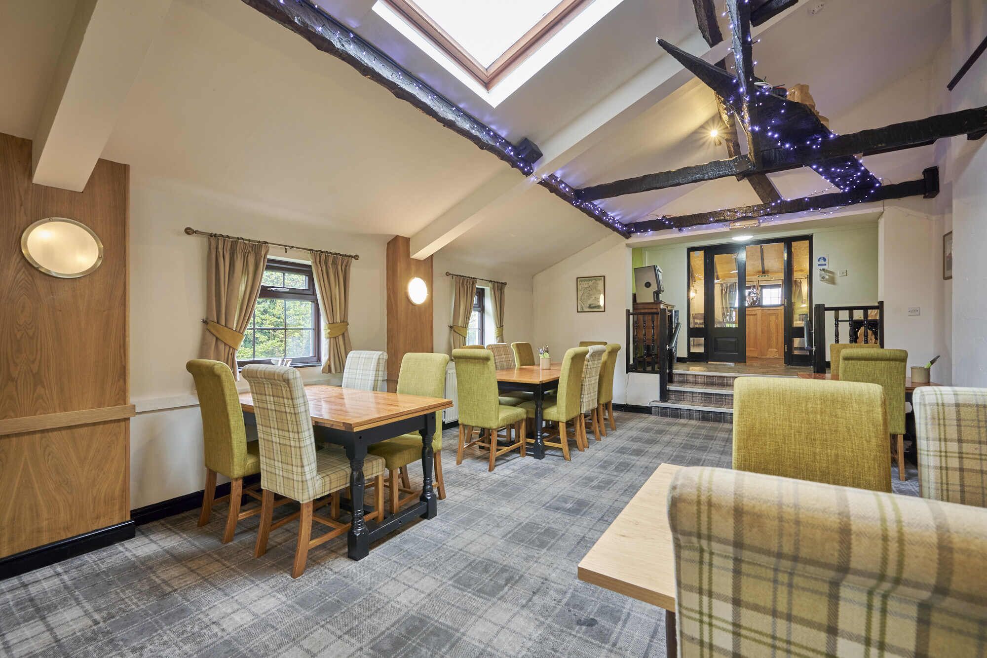 A dining area with a high ceiling, exposed beams, and a view of the kitchen through an open door.