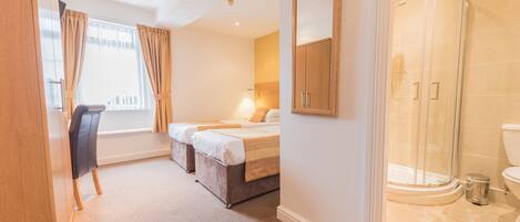 A hotel room with a bed, a desk, a chair, a shower, and a toilet.
