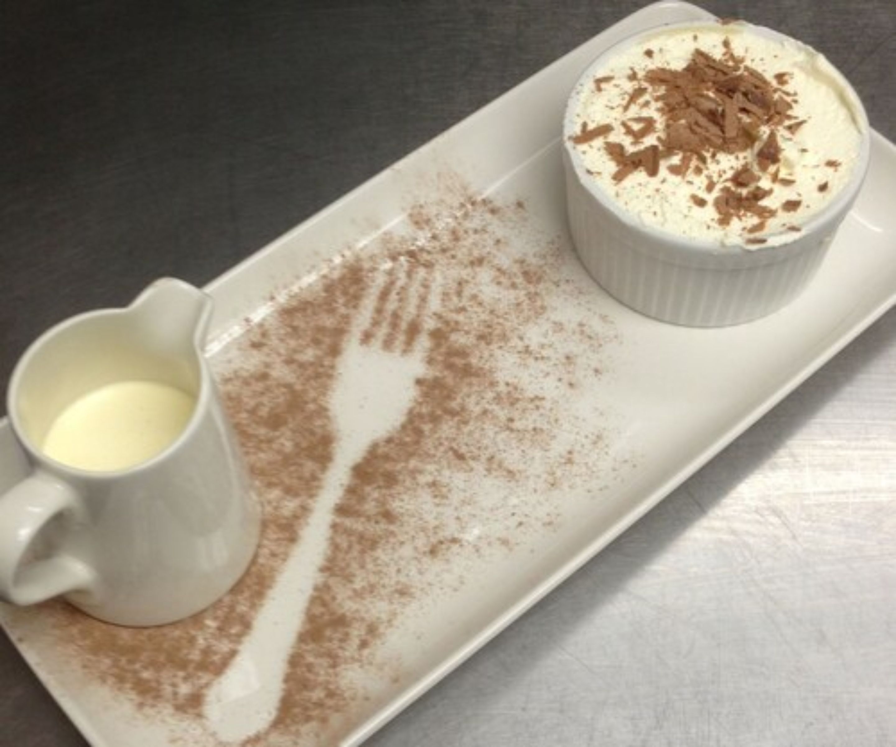 Sobremesa com chantilly e raspas de chocolate sobre um prato branco.