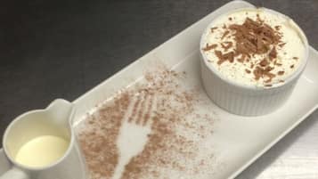 Sobremesa com chantilly e raspas de chocolate sobre um prato branco.