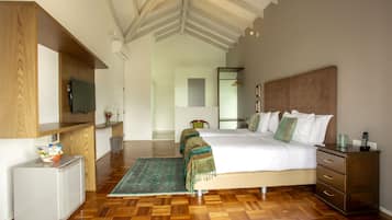 Una habitación de hotel con piso de madera, una cama con ropa blanca, un aparador de madera, un escritorio pequeño con un televisor y un espejo en la pared.
