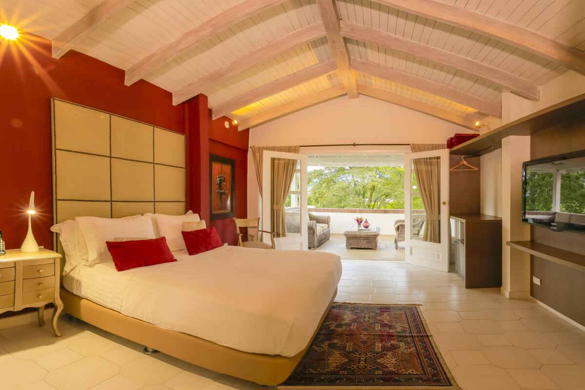 Un dormitorio amplio con una cama grande, televisión y balcón con mobiliario de mimbre.