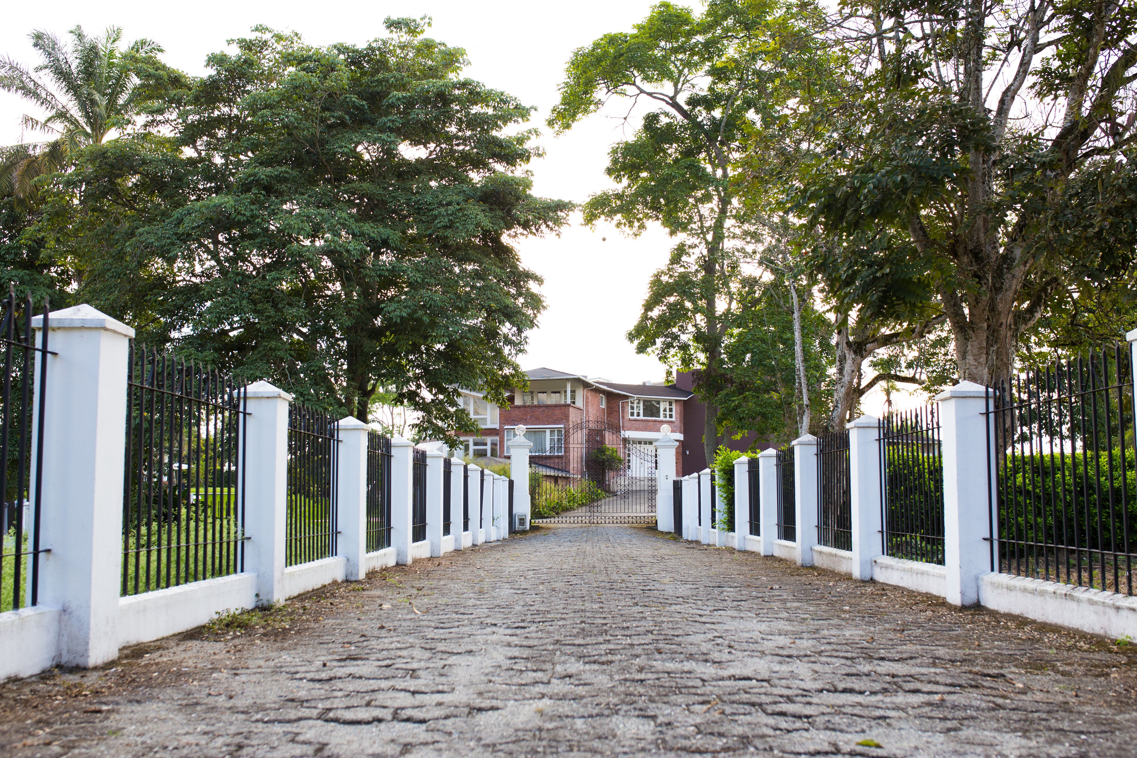 Un sendero adoquinado que conduce a una entrada porticada con pilares blancos y valla de metal negro.
