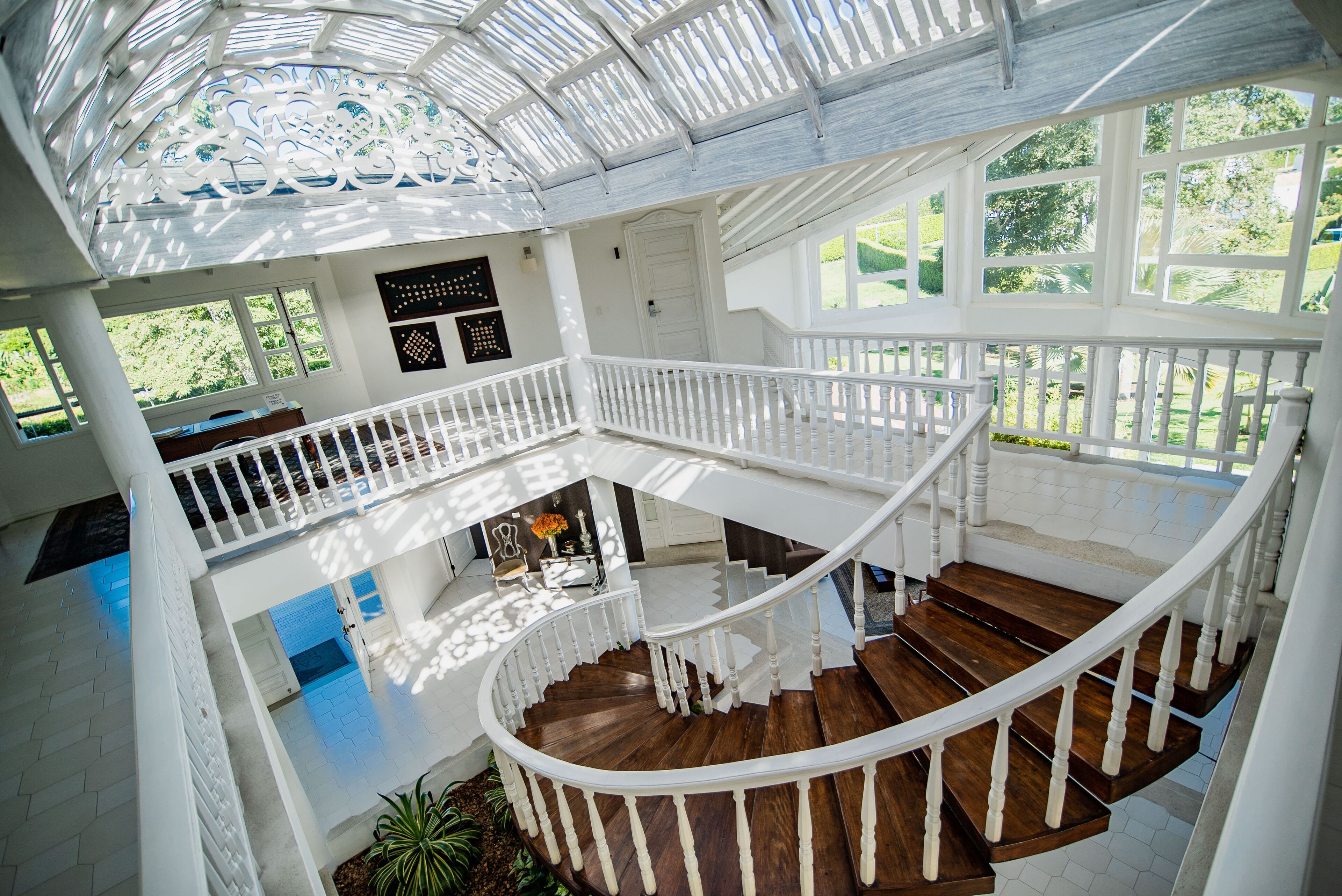 Un interior espacioso de varios niveles con una escalera de madera, barandas blancas y grandes ventanales que dan a vistas del jardín.
