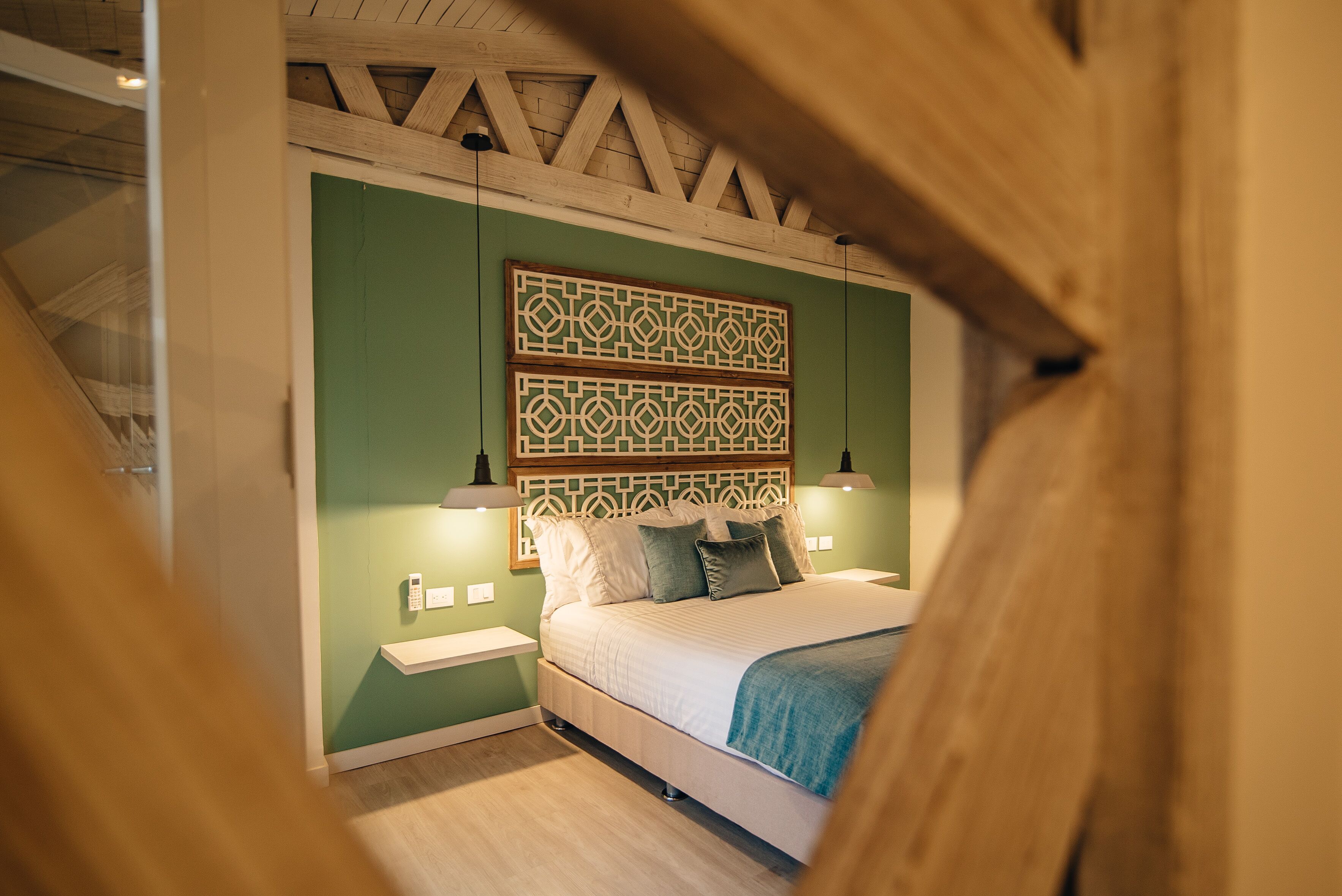A bedroom with a bed, green walls, wooden ceiling beams, and two bedside lamps.