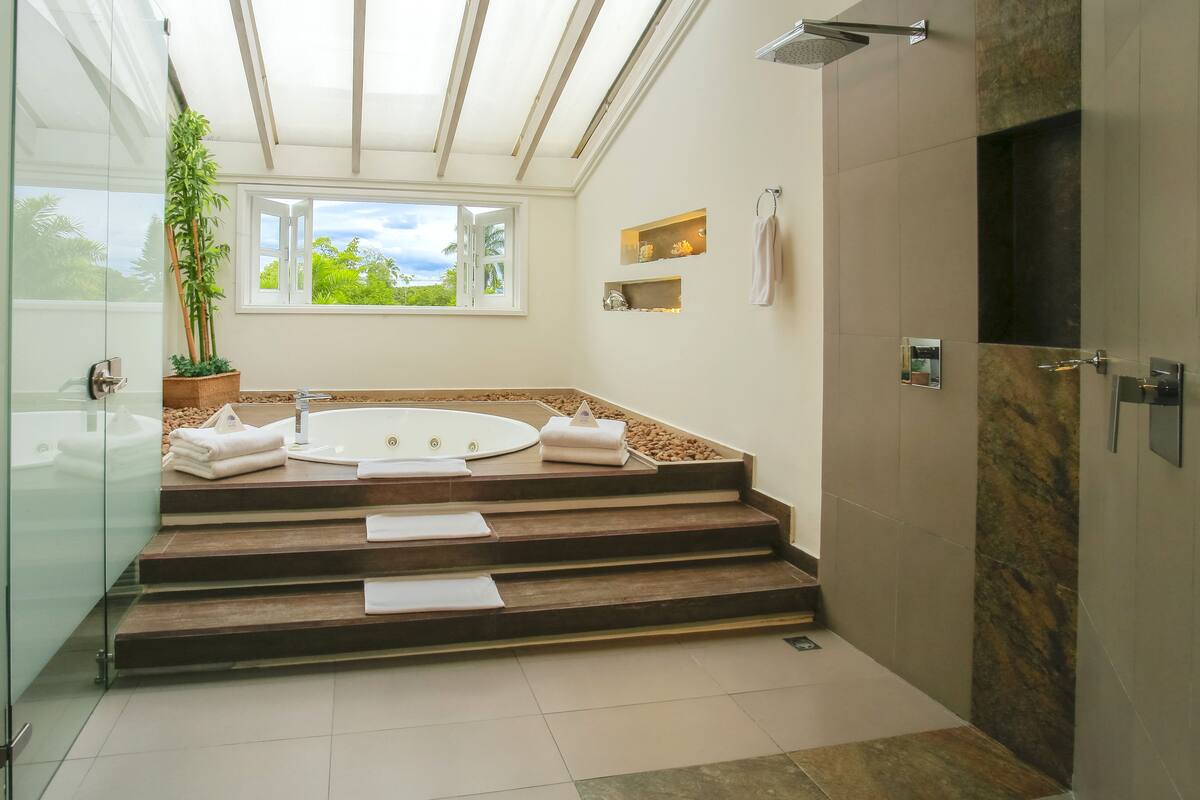 Un baño moderno con una bañera independiente, un box de ducha de cristal y vistas a zonas verdes.