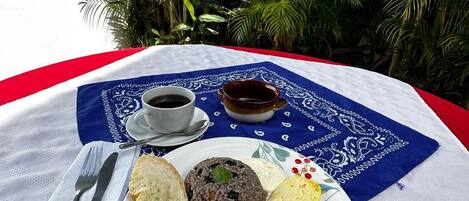 Un plato de desayuno con tostadas, huevos revueltos, salchichas y un plato de arroz, servido sobre un plato blanco con una servilleta azul y un mantel blanco.