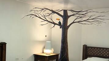 Habitación de hotel con dos camas de madera, una mesita de noche con lámpara y un mural de un árbol en la pared.