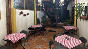 Un área de comedor al aire libre con mesas y sillas, una escalera y lámparas colgantes.