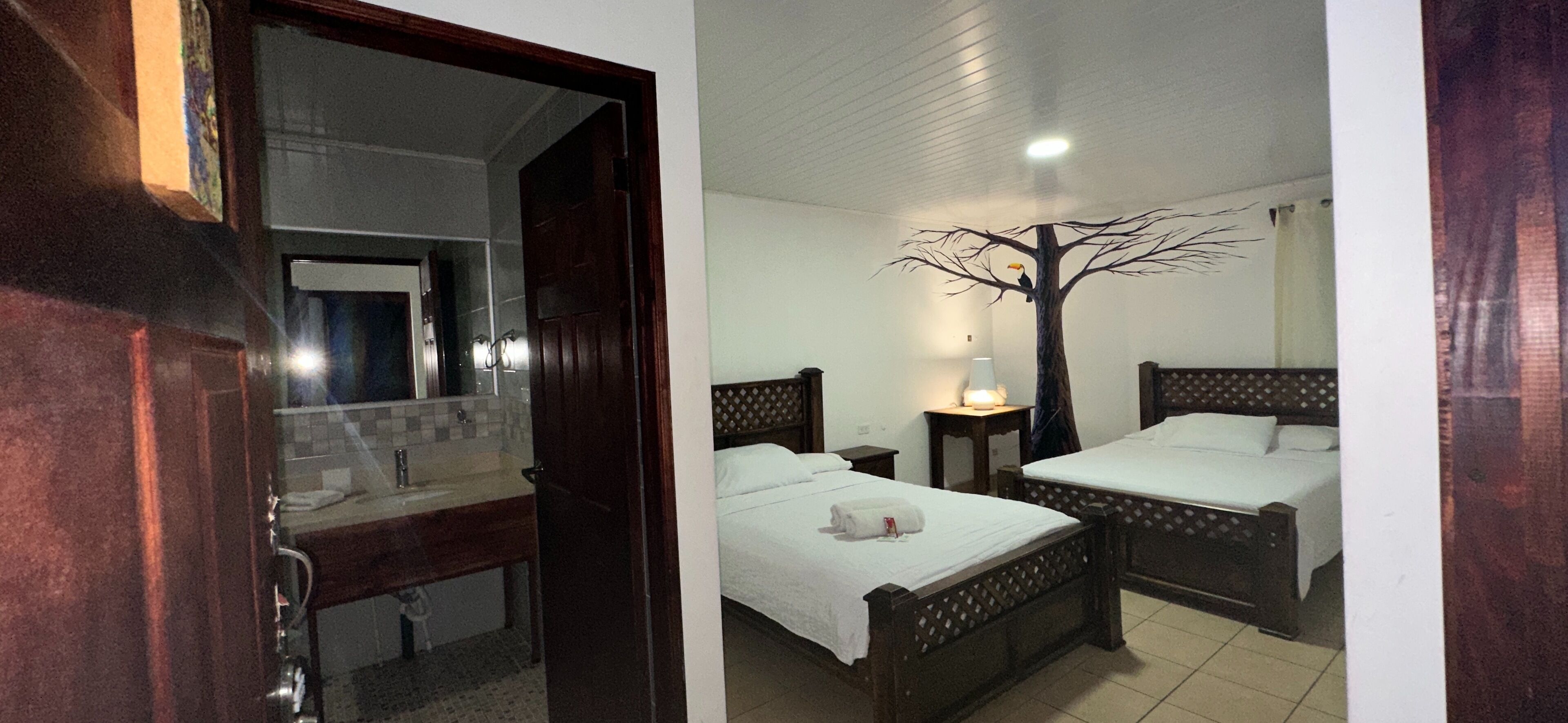 Una habitación de hotel con dos camas individuales, un cabecero de madera, una mesita de noche, una lámpara y un espejo.
