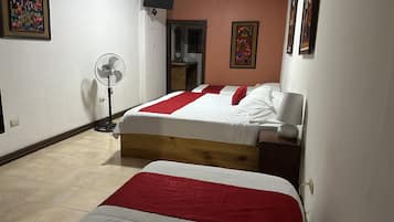 A bedroom with two beds, a standing fan, and a television on the wall.