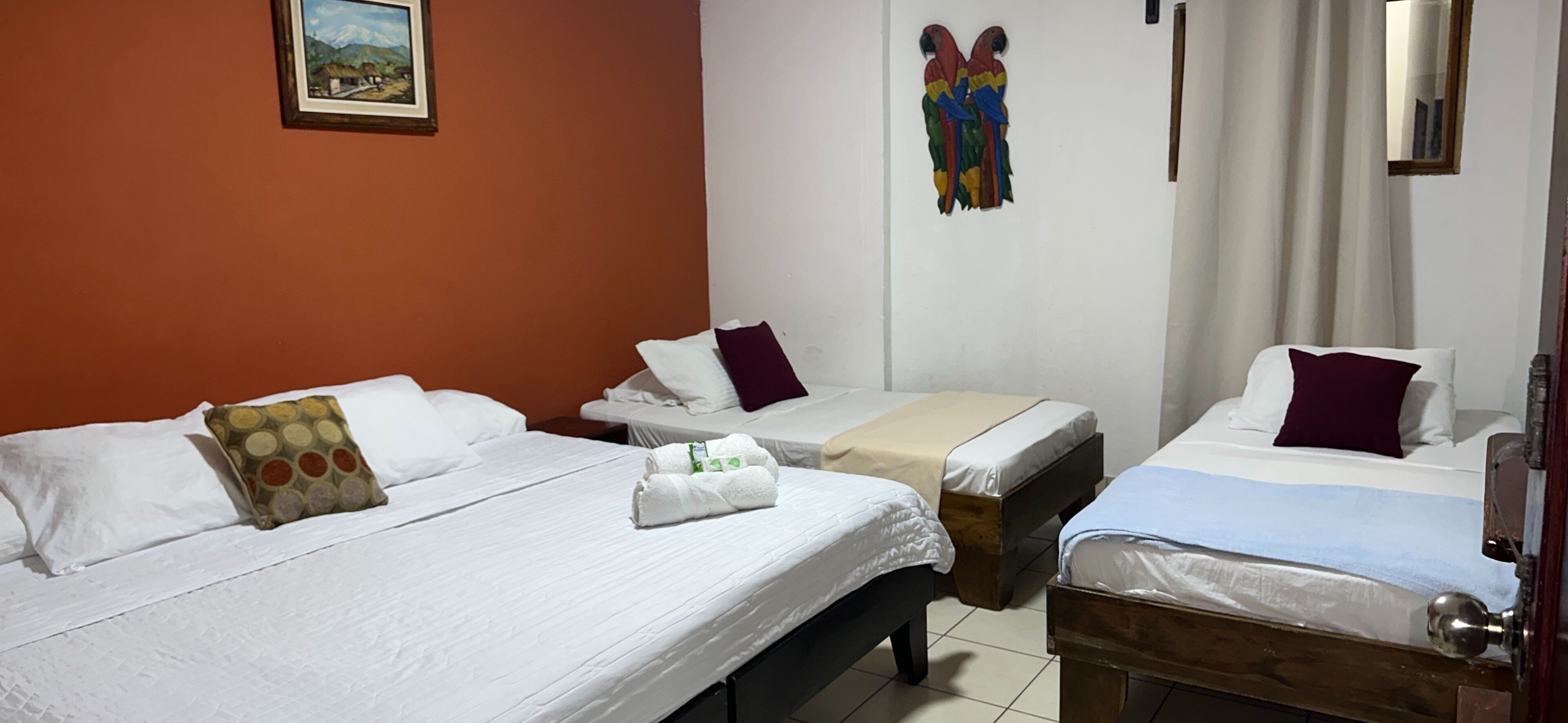 Habitación de hotel con dos camas, cada una con sábanas y almohadas blancas, cabeceros de madera y un cuadro en la pared.