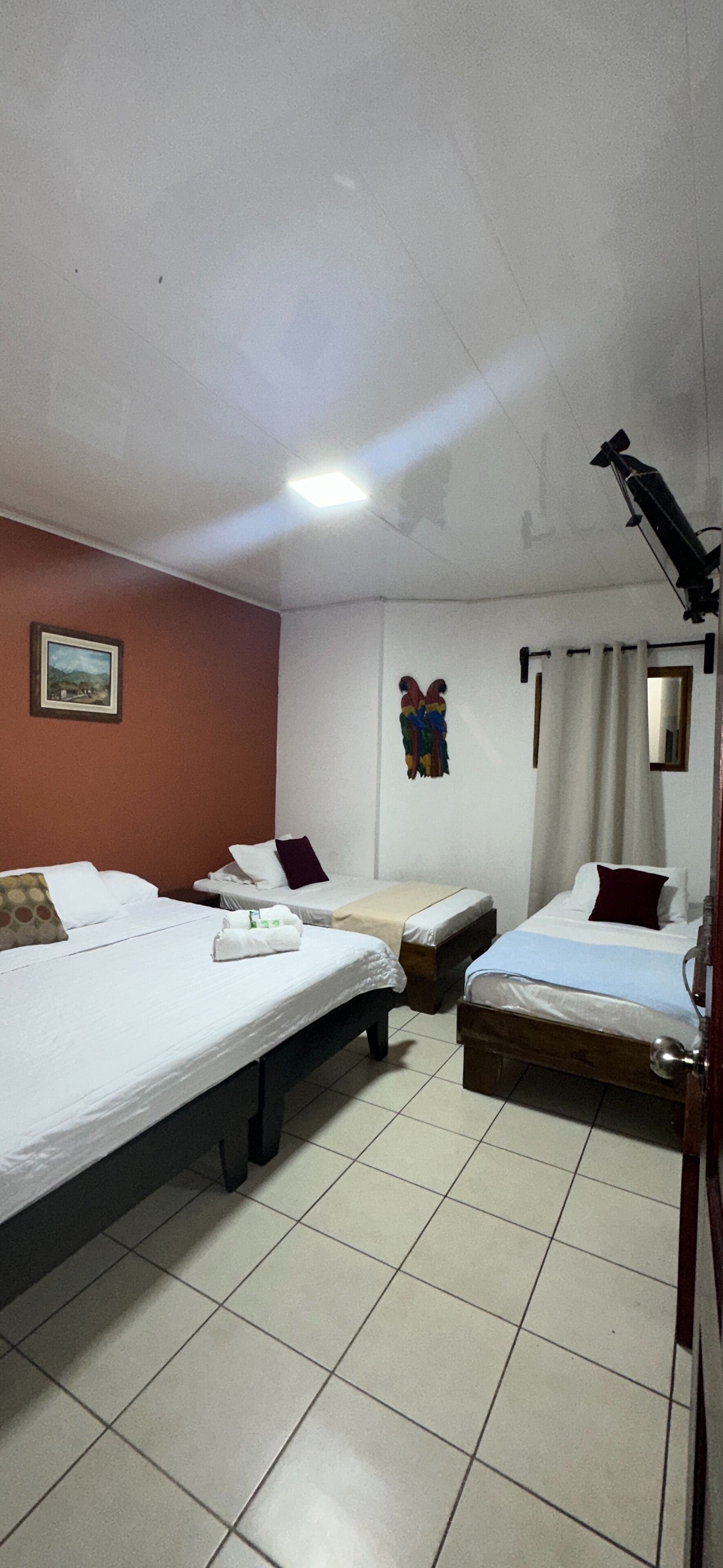 Une chambre d’hôtel avec deux lits simples, une petite table, une chaise, un miroir et un luminaire au plafond.