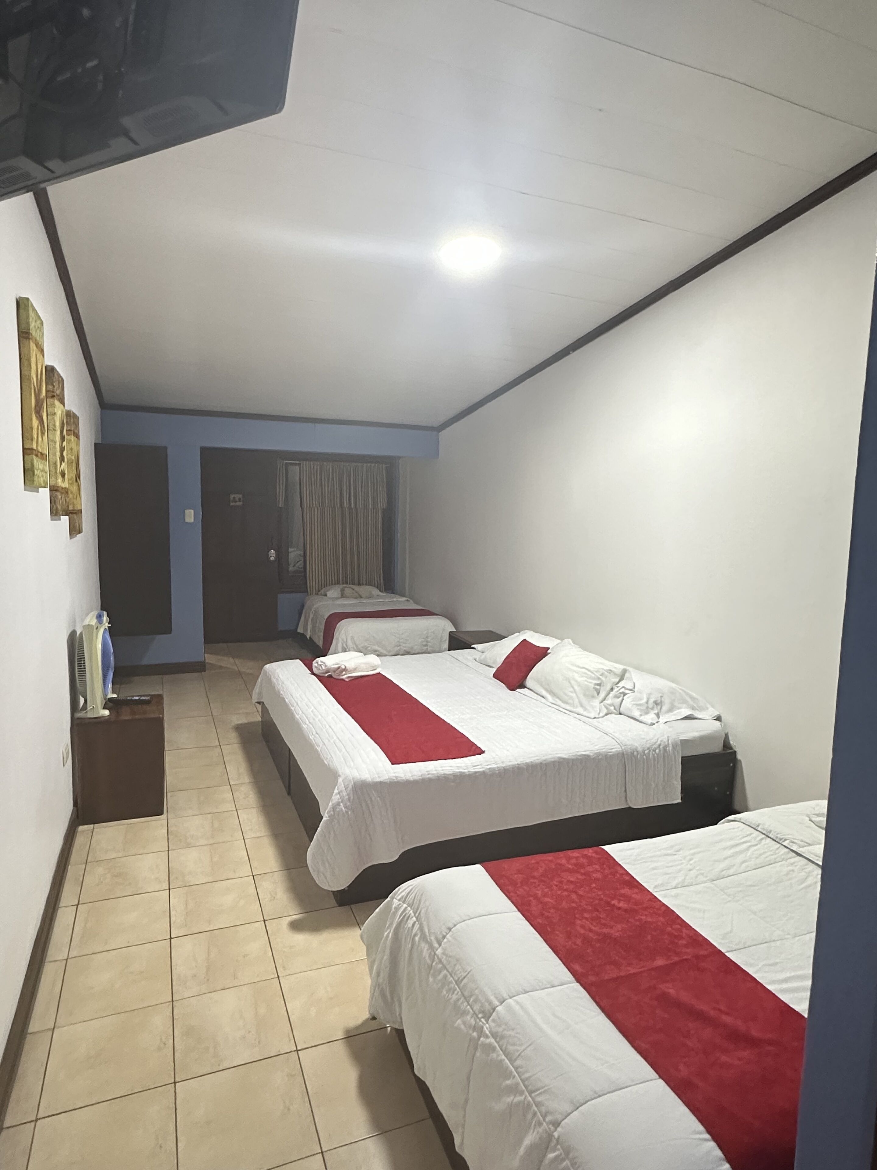 Ein Hotelzimmer mit zwei Betten, einem kleinen Schreibtisch und einem an der Wand befestigten Fernseher.