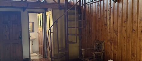 A wooden cabin with a bed, a staircase, and a bathroom.