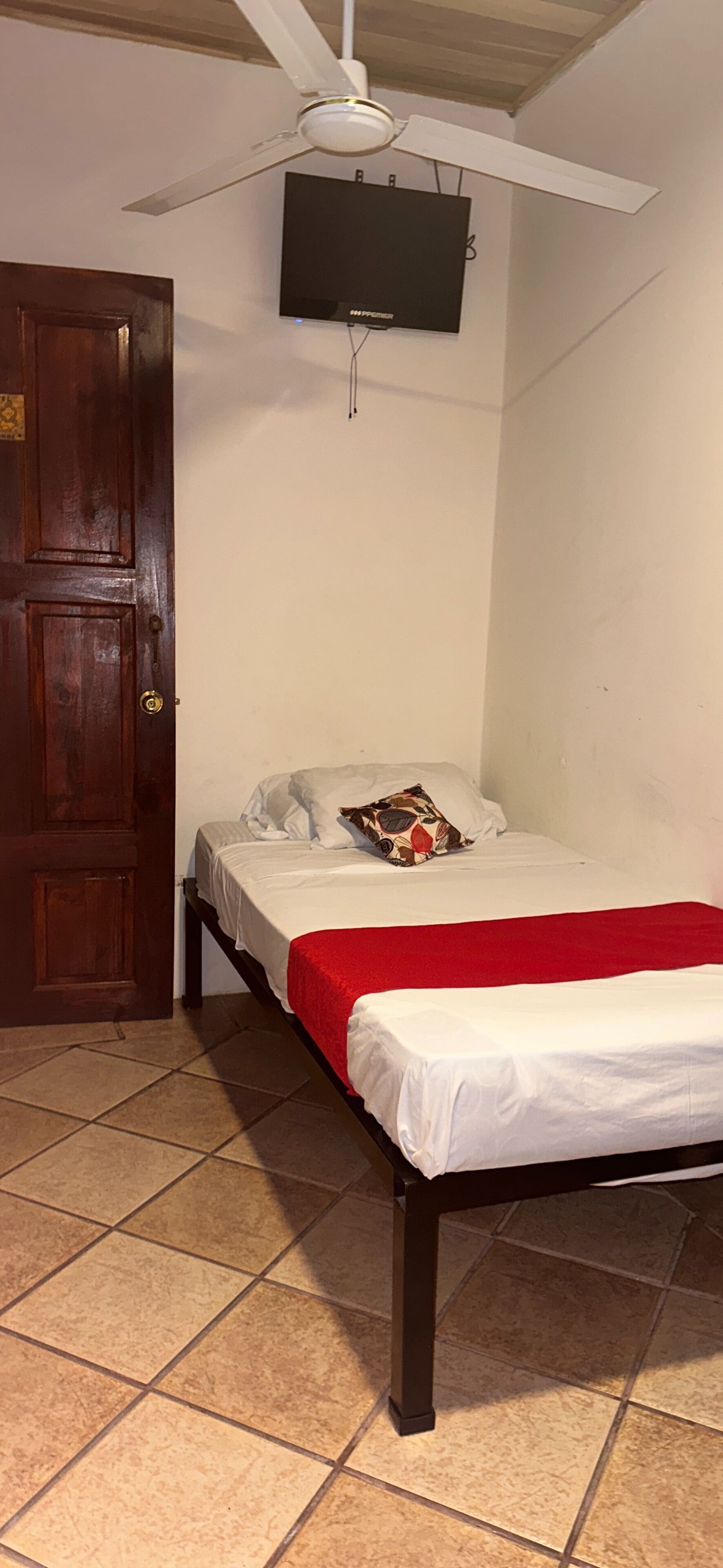 A bedroom with a bed, a red blanket, a wooden door, and a ceiling fan.