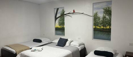 Una camera d'albergo con due letti singoli, un'ampia finestra vista alberi e lago, e una luce a soffitto.