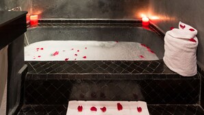 Un baño con bañera, velas y pétalos de rosa.