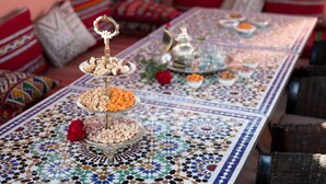 Una larga mesa ornamentada con un detallado patrón de mosaico, ubicada en una habitación con cojines de estilo marroquí tradicional y una rosa roja.