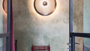 Una habitación con una pared texturizada, un banco con un cojín estampado, un otoman amarillo y un par de zapatillas en el suelo.