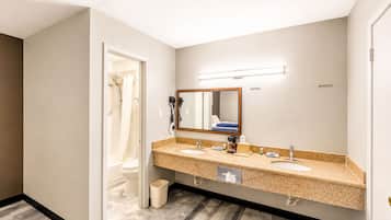 A hotel bathroom with a double sink, a mirror, a hairdryer, and a shower.