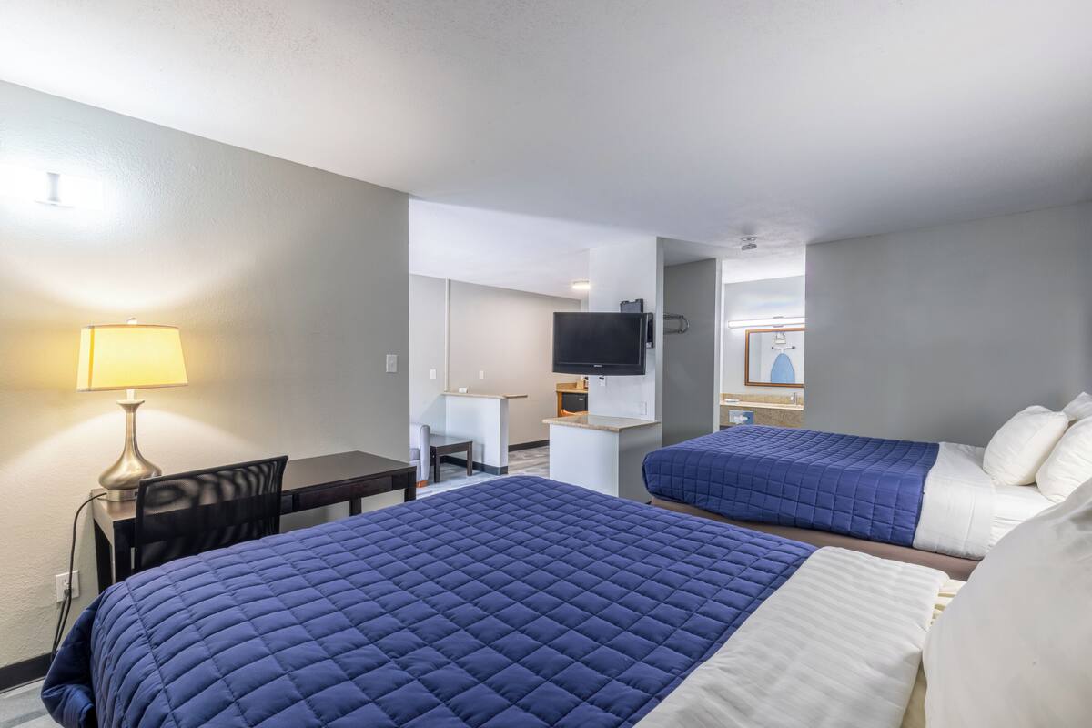 A hotel room with two beds, a desk, a chair, a TV, and a lamp.