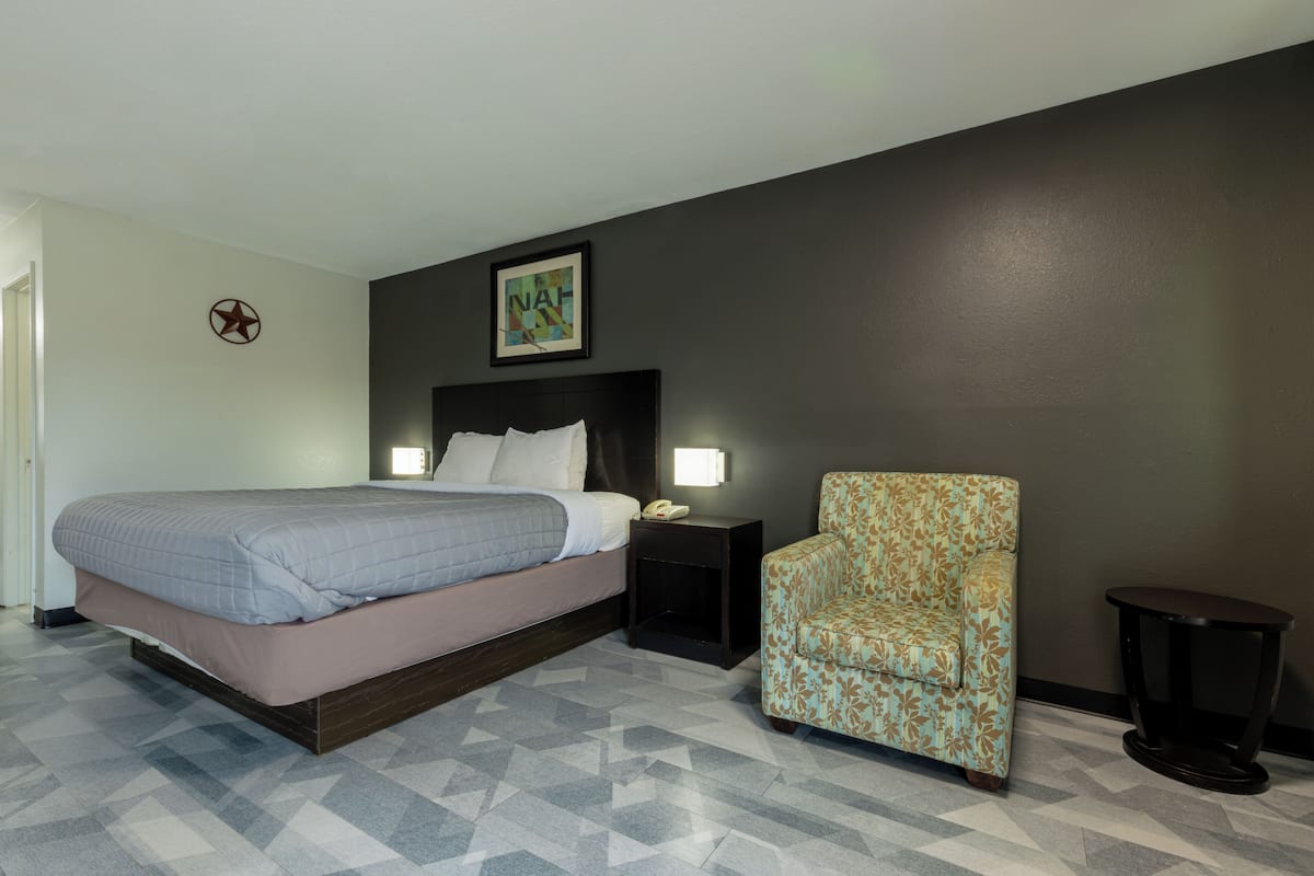 A hotel room with a bed, a chair, a nightstand, and a wall-mounted phone.