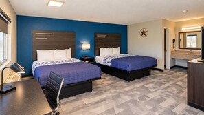 A hotel room with two beds, a desk, a chair, a nightstand, a lamp, a star decoration, and a bathroom with a mirror. - Freer Executive Inn and Studios (Freer)