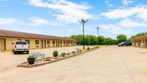 A motel with a parking lot, a row of rooms, and a central walkway with benches and planters. - Freer Executive Inn and Studios (Freer)