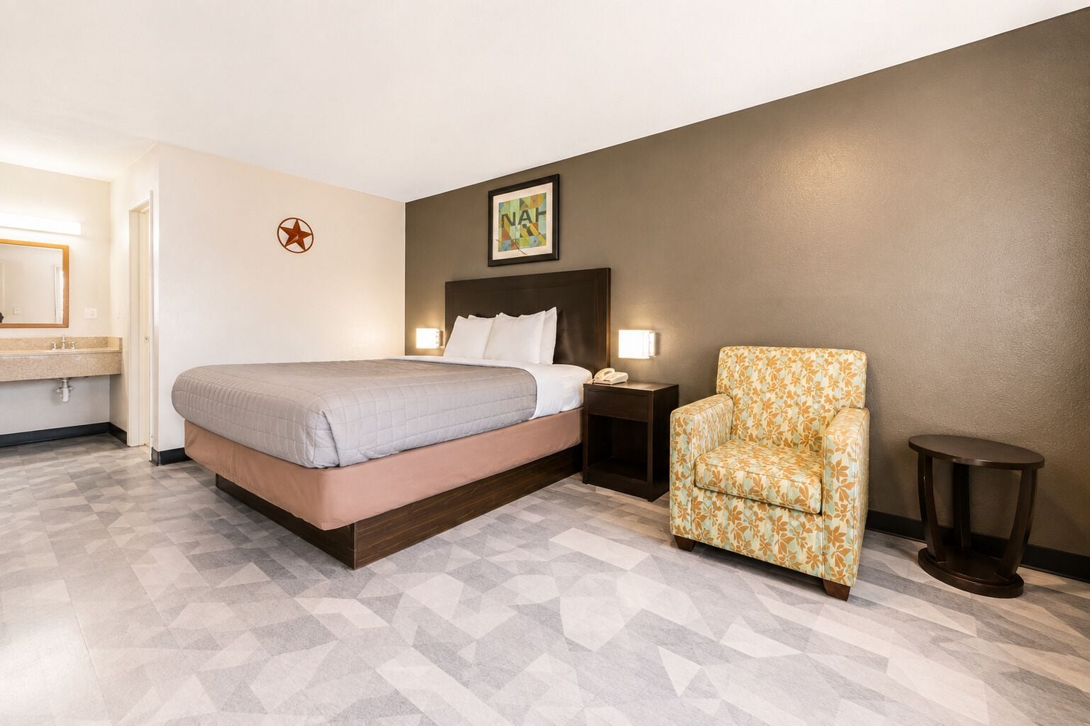 A hotel room with a bed, a chair, a nightstand, and a small table.