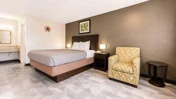 A hotel room with a bed, a chair, a nightstand, and a small table.