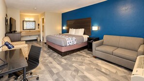 Habitación de hotel con cama, sofá, escritorio con silla, televisor y baño.