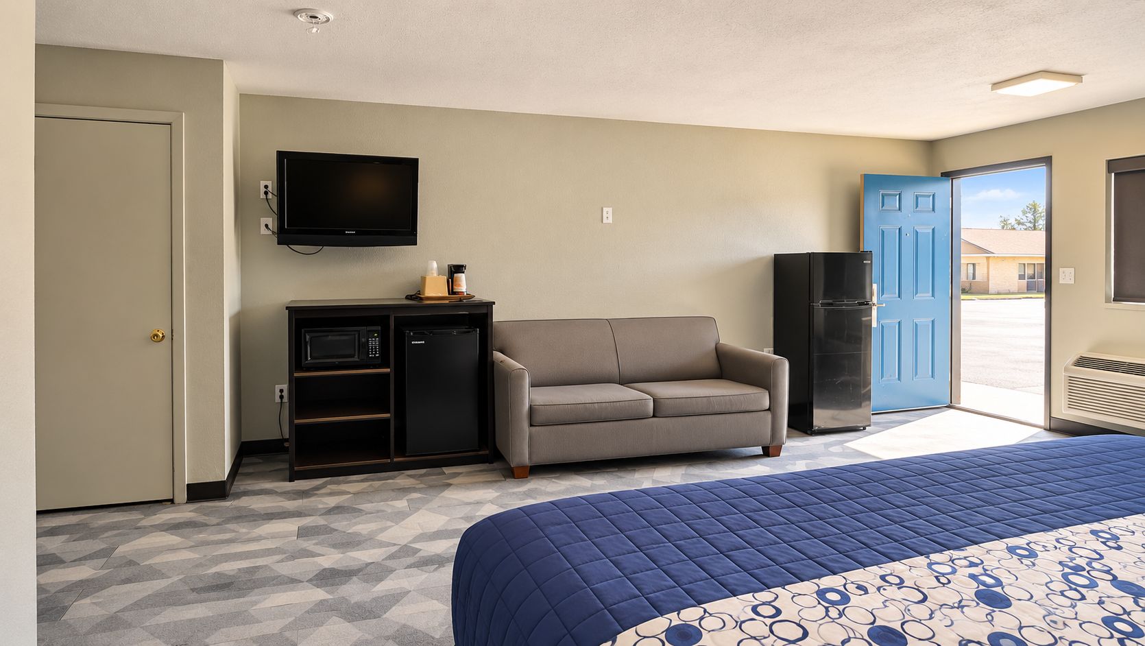 Habitación de hotel con cama, sofá, televisión, kitchenette y puerta que da al exterior.