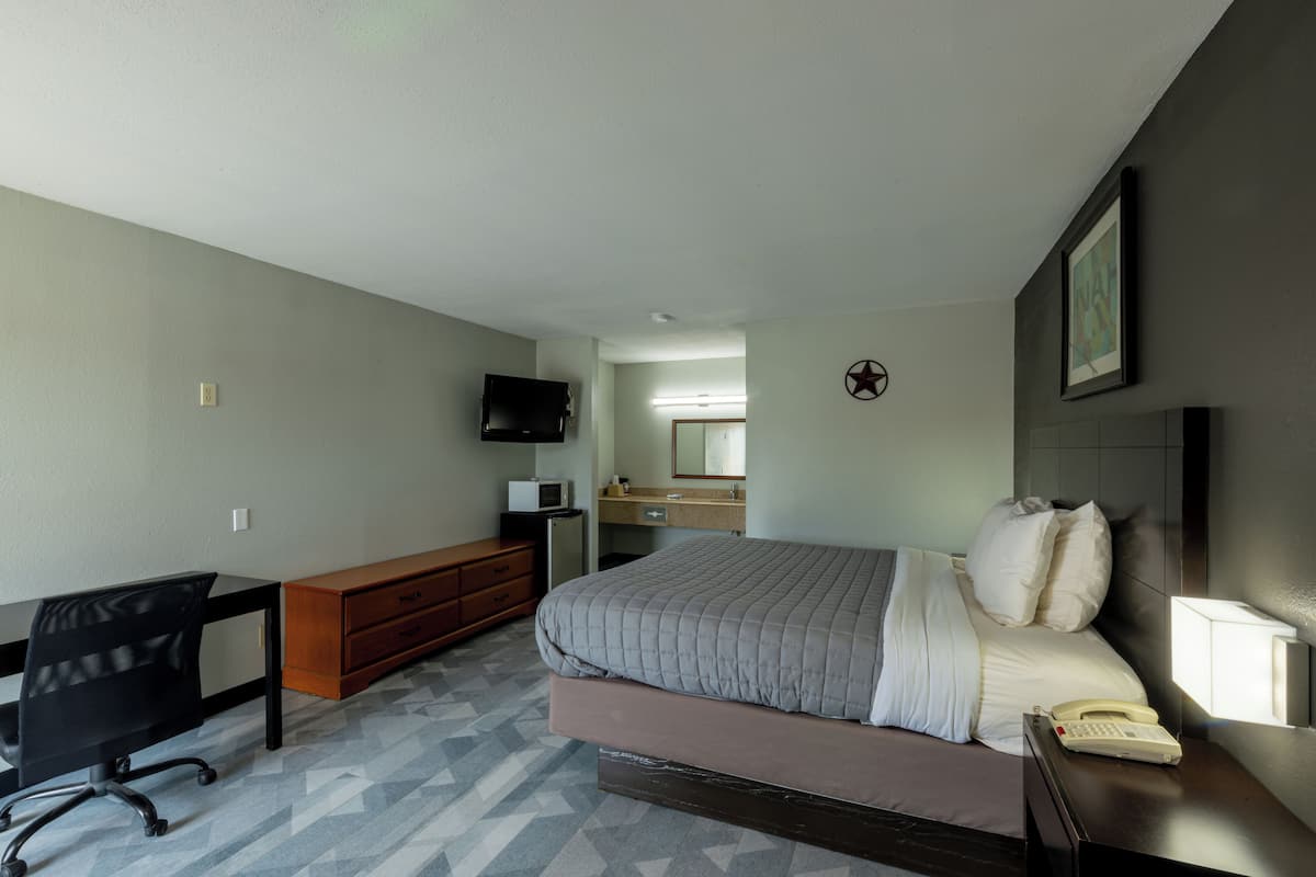 A hotel room with a bed, desk, chair, dresser, and a television.