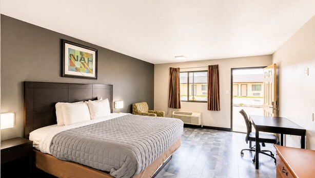 A hotel room with a bed, a desk, a chair, and a window. - Freer Executive Inn and Studios (Freer)