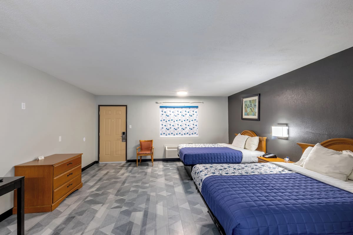 A room with two beds, a dresser, a chair, a window with a blue and white pattern, and a painting on the wall.