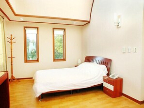 Una camera da letto con un letto di legno, due finestre, un comodino con un telefono e un appendiabiti.