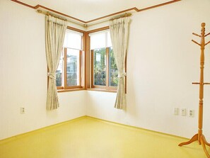 Una stanza con due finestre, un appendiabiti in legno e un pavimento giallo.