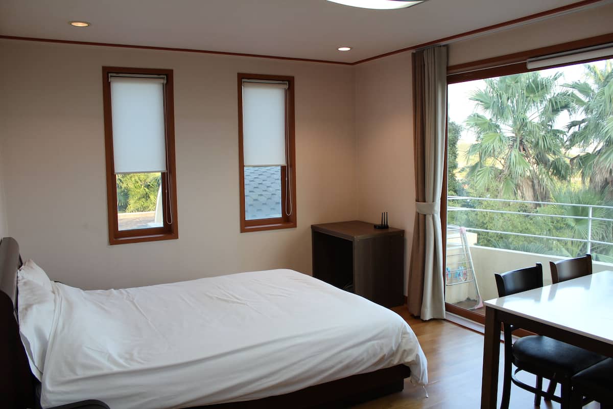 Ein Schlafzimmer mit Bett, Tisch, Stühlen und einem Balkon mit Blick auf Palmen.