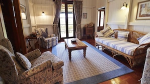 Una sala de estar acogedora con un sofá, un sillón y una pequeña mesa. Hay una puerta con cortinas, una lámpara de pared y una alfombra en el suelo.