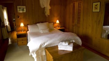 Un dormitorio con paneles de madera, una cama, dos mesitas de noche con lámparas, una mesita auxiliar y una banca de madera, además de una puerta con ventanal.