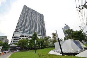 Un edificio alto y moderno con un diseño arquitectónico único, rodeado por un parque bien cuidado con un elemento acuático.